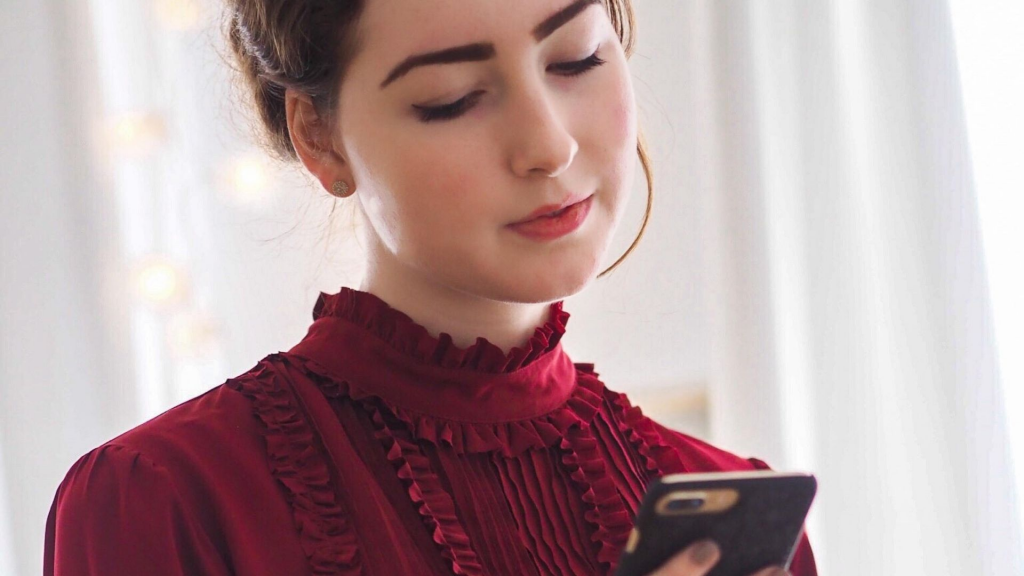 A woman in a European couture dress looking down at a smartphone.